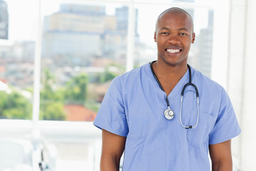 African American doctor standing smiling in clinic wearing blue scrubs with stethoscope, copy space