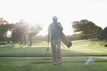 Golf bag resting on manicured fairway during sunrise with lens flare through scattered trees