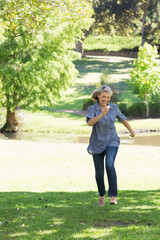 Woman running across grass in sunny park near pond wearing sunglasses on head and slip-on shoes