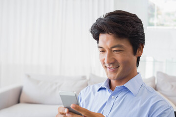 Japanese man in shirt using smartphone on white sofa, neutral cushions in living room, copy space