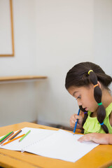 Schoolgirl drawing in notebook with colored pencils at school desk wearing green top, copy space