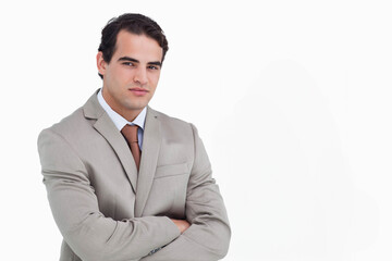 Male standing with arms crossed in studio wearing light gray suit and brown tie, copy space