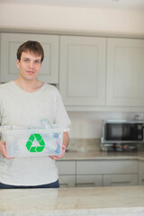 Man in his thirties holding recycling bin full of bottles on countertop, copy space