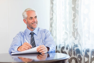 Man in dress shirt and tie writing documents at wooden table by window, copy space
