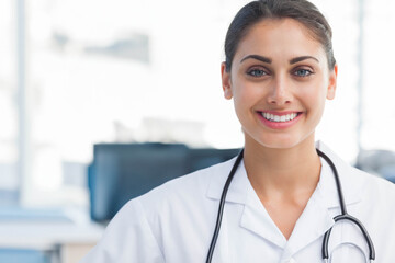 Smiling female doctor wearing lab coat and stethoscope in clinic with computer monitors, copy space