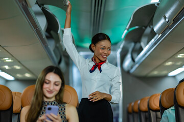 Flight hostess checking and closing luggage bins during routine flight boarding procedures while looking and talking with passenger with service mild.