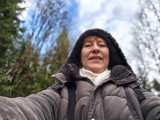 Mature woman enjoys a winter excursion in a forest while capturing a selfie for her lifestyle blog