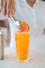 Professional bartender adding a final touch to a vibrant orange cocktail by carefully placing a...