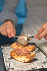 Professional chef working in restaurant kitchen adding spices and seasoning to raw meat appetizer on toasted bread, preparing delicious dish