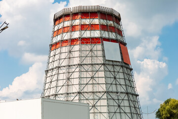 A tall cylindrical cooling tower with a metal frame, painted white and red. Against the backdrop of...