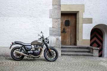 Matte Black Motorcycle on Cobblestone Street Beside Old Building With Wooden Door