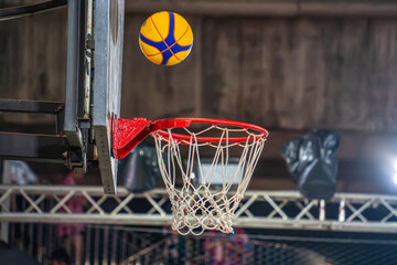A yellow and blue basketball is caught in motion just above the hoop during an indoor game.