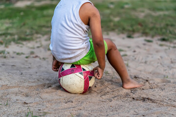 Boy sitting, playing soccer ball on the sand.