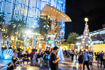 Night scene with people walking under blue and yellow holiday lights, with a Christmas tree in view.