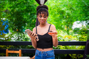 An African woman looks confused or frustrated while checking her credit card and holding her phone,...