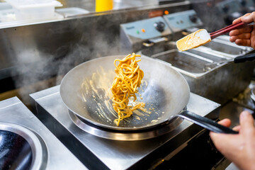 Professional chef stir-frying noodles in a wok with steam rising, showcasing dynamic motion and...
