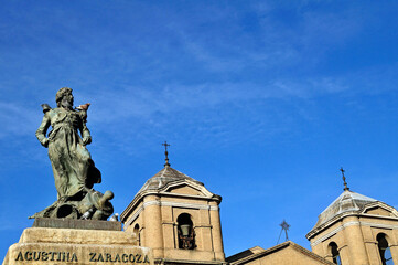 Fototapeta premium Statue of Agustina Zaragoza with pigeon and church bell towers in Zaragoza, Spain