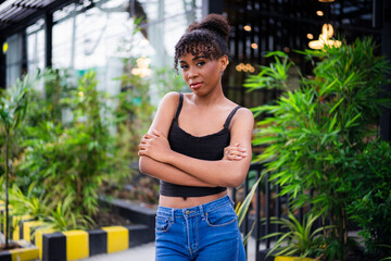 Stylish African woman in black crop top and jeans standing with arms crossed outside a modern...