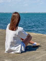 A young woman relaxes by the water, enjoying a tranquil moment against a backdrop of shimmering...