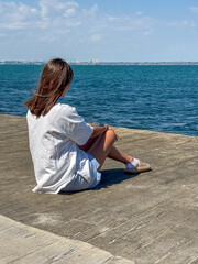 Young woman enjoying a serene moment by the water, dressed in a casual outfit with a peaceful...