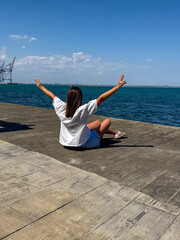 A young Hispanic woman enjoys a sunny day by the waterfront, celebrating the moment with arms...