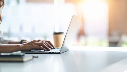 Close-up of a woman's hands typing on a laptop at a desk by a sunny window.