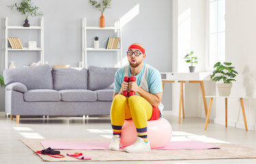 Funny beginner man in retro sportswear and glasses is exercising at home. His amazed demeanor and...