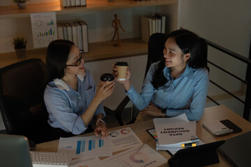 Celebrating Small Wins. Two women toasting with coffee cups during a late-night work session.