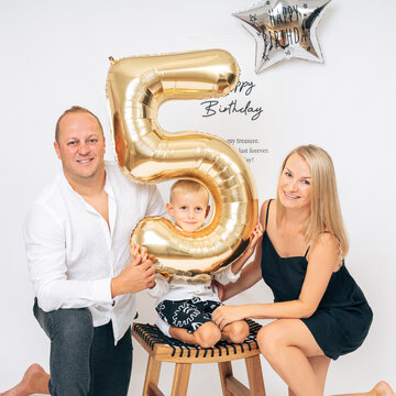 Happy family celebrating chils 5th birthday with golden balloon