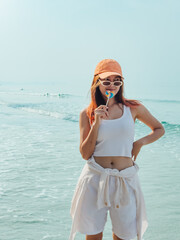 Young woman with colorful lollipop and orange hat enjoy the beach.