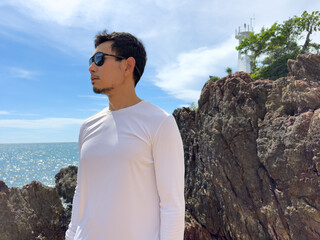 Side view of Asian man in white shirt by rocky seaside