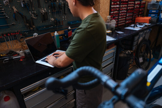 Bicycle mechanic using laptop in repair shop, searching spare parts - Powered by Adobe