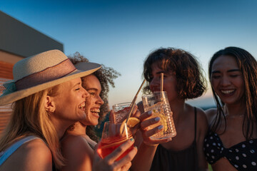 Group of friends toasting cocktails at sunset rooftop party