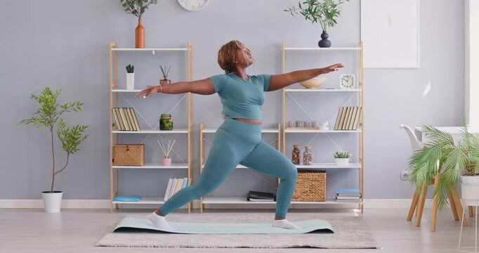 Fat, plus size African American woman wearing sportswear practicing yoga training at home. Doing sport, fitness exercise, active lifestyle, wellness and workout in the comfort of home gym.