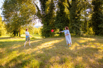 Caucasian mom and daughter throwing frisbee and smiling on grass in city park. Family bonding, real...