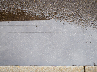 Abstract wet pavement with reflective water and rough concrete texture creating a textured surface...