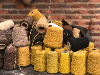 A vibrant pile of pure wool yarn cones in earthy tones like yellow, black, beige, and brown. Ideal...