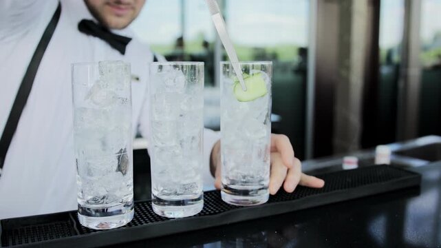 Bartender places cucumber in glasses with ice to make a cocktail, close-up, slow motion