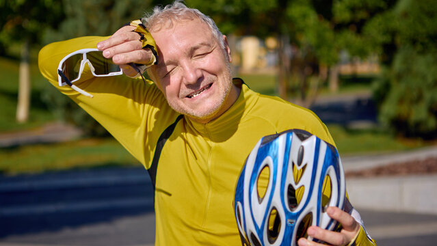 Elderly male cyclist wiping sweat with glove after intense ride. Concept of senior fitness awareness, health campaigns, active aging, and lifestyle promotion.