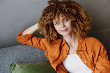 Stylish woman with curly hair in an orange shirt, smiling confidently, promoting natural beauty and...