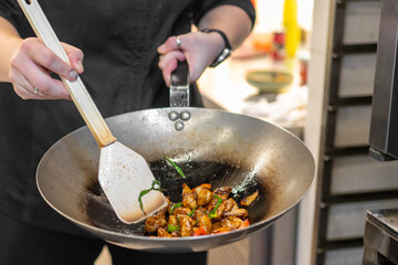 Chef stir-frying meat and vegetables in a wok, using a spatula. Colorful, appetizing dish in a...