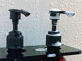 Foamy Dispenser Duo Black Bottles with Soap Bubbles in a Wet Bathroom Setting.