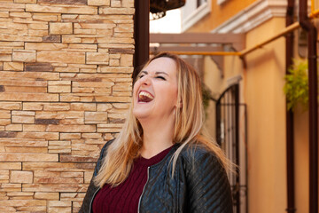 Fototapeta premium Photo shoot of a blonde woman in a black leather jacket and a burgundy sweater in the center of the city