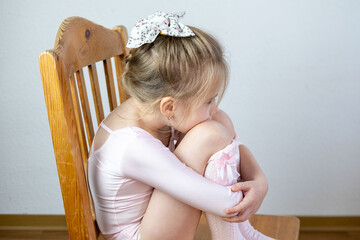Preschool ballerina in pink dress hugs knees, quiet moment, emotional expression, waiting or...