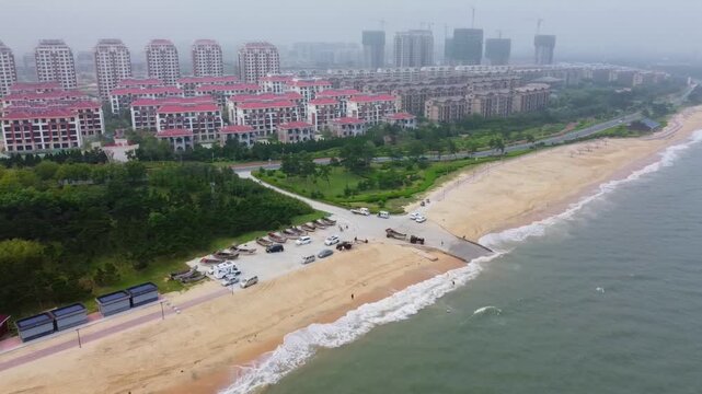 Nanhai Beach and cityscape view from left panning in Nanhai New District, Shandong Province, China. The crowded beach and basket-shaped monument.