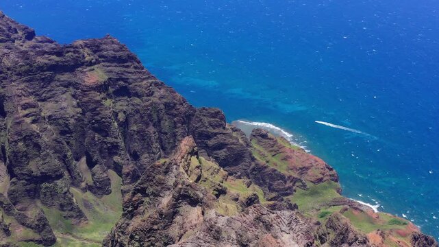 Drone shot looking down at Nu'lolo Aina Valley from Awa'awapuhi Trail on the Na Pali Coast in Kauai. Includes a boat in the blue waters of the Pacific Ocean, lush valley and rocky, mountain ridges.