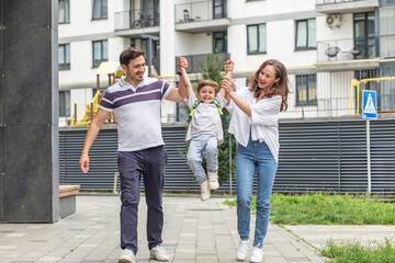Happy parents swinging son while walking outside. Back to school