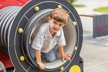Curious boy crawling out of playground tunnel