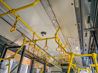 Interior view of public bus showing yellow handrails and grab handles on ceiling. Modern city...
