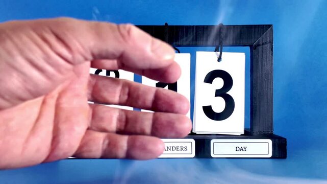 Left hand of an elderly person revealing a tear off calendar showing the date of August 13, international left handers day, isolated on a blue background